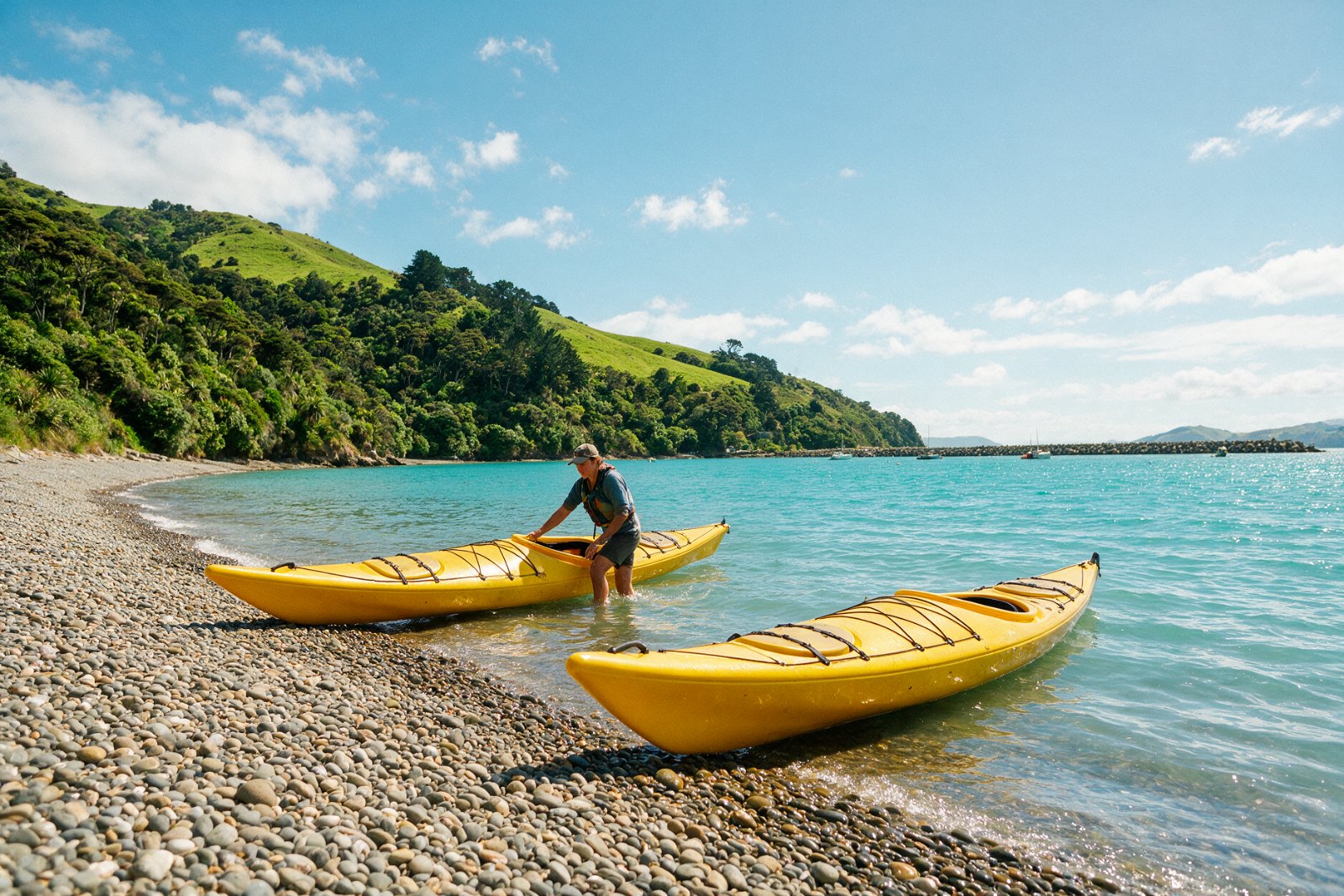 Guide launching yellow kayaks into a turquoise harbour